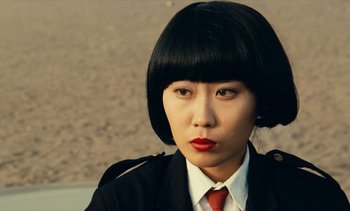 Movie still from “Hyenas” (1992), directed by Djibril Diop Mambéty – A woman in a black jacket and a red tie; Close Up shot, Over the shoulder angle