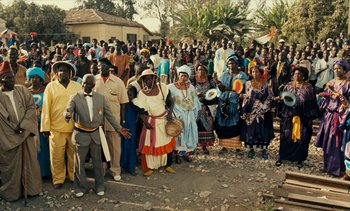 Movie still from “Hyenas” (1992), directed by Djibril Diop Mambéty – A large group of people standing in a street; Extreme Wide shot, High angle