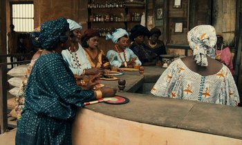 Movie still from “Hyenas” (1992), directed by Djibril Diop Mambéty – A group of women sitting at a counter; Medium shot, Over the shoulder angle