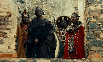 Movie still from “Hyenas” (1992), directed by Djibril Diop Mambéty – A group of people dressed in traditional african clothing; Medium shot, Low angle