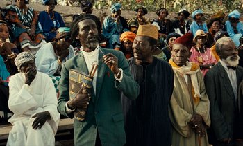 Movie still from “Hyenas” (1992), directed by Djibril Diop Mambéty – A group of men standing next to each other in a crowd; Medium shot, Over the shoulder angle
