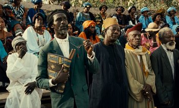 Movie still from “Hyenas” (1992), directed by Djibril Diop Mambéty – A group of people standing in front of a group of people; Medium shot, Low angle
