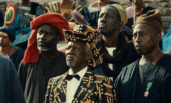 Movie still from “Hyenas” (1992), directed by Djibril Diop Mambéty – A group of men standing next to each other; Medium shot, Low angle