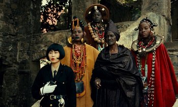 Movie still from “Hyenas” (1992), directed by Djibril Diop Mambéty – A group of people dressed up in costumes; Medium shot, Low angle
