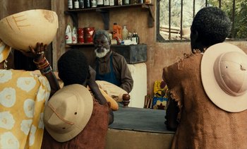 Movie still from “Hyenas” (1992), directed by Djibril Diop Mambéty – An old man sitting at the counter of a store; Medium shot, Over the shoulder angle