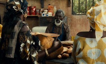 Movie still from “Hyenas” (1992), directed by Djibril Diop Mambéty – An older man sitting on a couch next to a woman; Medium shot, Over the shoulder angle