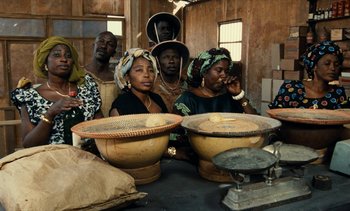 Movie still from “Hyenas” (1992), directed by Djibril Diop Mambéty – A group of people standing around a table; Medium shot, High angle