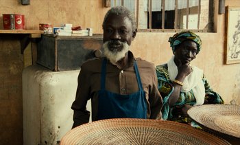 Movie still from “Hyenas” (1992), directed by Djibril Diop Mambéty – An older man and woman standing next to each other; Medium shot, Over the shoulder angle