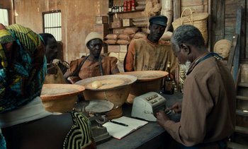 Movie still from “Hyenas” (1992), directed by Djibril Diop Mambéty – A group of people sitting at a table with pots; Medium shot, High angle