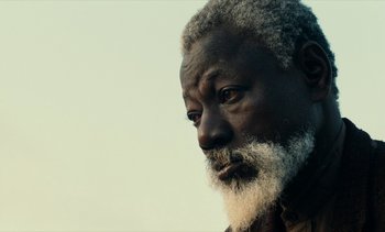 Movie still from “Hyenas” (1992), directed by Djibril Diop Mambéty – An old man with a beard and a white beard; Close Up shot, Low angle
