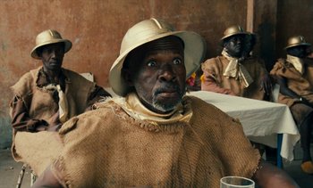 Movie still from “Hyenas” (1992), directed by Djibril Diop Mambéty – A group of men sitting around a table; Close Up shot, Over the shoulder angle