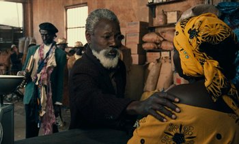 Movie still from “Hyenas” (1992), directed by Djibril Diop Mambéty – An older man and a woman in a room; Medium shot, Over the shoulder angle