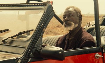 Movie still from “Hyenas” (1992), directed by Djibril Diop Mambéty – An older man sitting in a car looking out of the window; Close Up shot, Over the shoulder angle