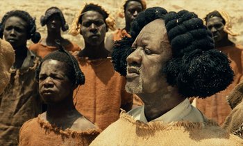 Movie still from “Hyenas” (1992), directed by Djibril Diop Mambéty – A group of people standing in a field; Close Up shot, Over the shoulder angle