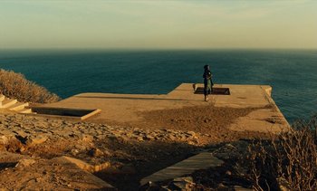 Movie still from “Hyenas” (1992), directed by Djibril Diop Mambéty – A person standing on a beach near the ocean; Extreme Wide shot, High angle