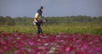 Movie still from “Jason's Lyric” (1994), directed by Doug McHenry – A man carrying a child on his back in a field of flowers; Wide shot, Low angle