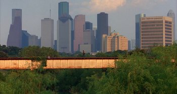 Movie still from “Jason's Lyric” (1994), directed by Doug McHenry – A person riding a bike over a bridge in the middle of a city; Extreme Wide shot, High angle