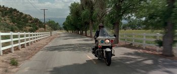 Movie still from “Johnson Family Vacation” (2004), directed by Christopher Erskin – A man riding a motorcycle down the middle of a road; Wide shot, Low angle