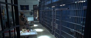 Movie still from “Johnson Family Vacation” (2004), directed by Christopher Erskin – A person sitting at a table in a jail cell; Wide shot, High angle