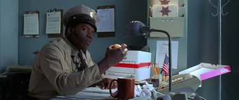 Movie still from “Johnson Family Vacation” (2004), directed by Christopher Erskin – A police officer sitting at a desk eating a donut; Close Up shot, High angle