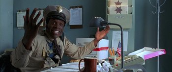 Movie still from “Johnson Family Vacation” (2004), directed by Christopher Erskin – A police officer sitting at a desk with a coffee mug; Medium shot, High angle
