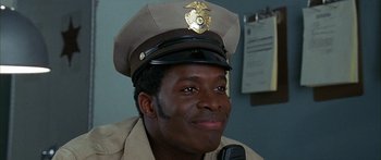 Movie still from “Johnson Family Vacation” (2004), directed by Christopher Erskin – A man in a police uniform smiles for the camera; Close Up shot, Low angle