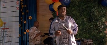 Movie still from “Johnson Family Vacation” (2004), directed by Christopher Erskin – A man holding a microphone in front of a bunch of balloons; Medium shot, High angle