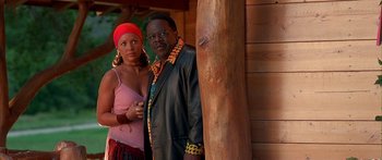 Movie still from “Johnson Family Vacation” (2004), directed by Christopher Erskin – A man and a woman standing next to each other in front of a wooden pole; Medium shot, Low angle
