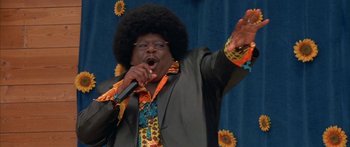 Movie still from “Johnson Family Vacation” (2004), directed by Christopher Erskin – A man in a black jacket and a wig is singing; Medium shot, Low angle