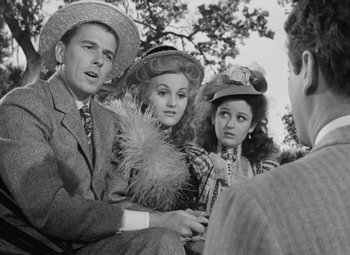 Movie still from “Kings Row” (1942), directed by Sam Wood – A man and two women sitting next to each other in front of another man; Medium shot, Over the shoulder angle