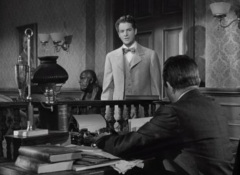 Movie still from “Kings Row” (1942), directed by Sam Wood – A black and white photo of a man in a suit and bow tie in a courtroom; Medium shot, Over the shoulder angle