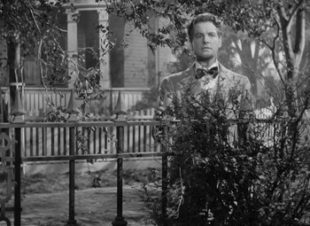 Movie still from “Kings Row” (1942), directed by Sam Wood – A black and white photo of a man standing in front of a fence; Medium shot, Low angle