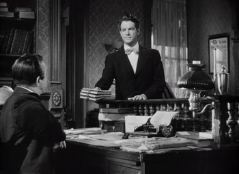 Movie still from “Kings Row” (1942), directed by Sam Wood – A black and white photo of a man standing at a desk; Medium shot, Low angle