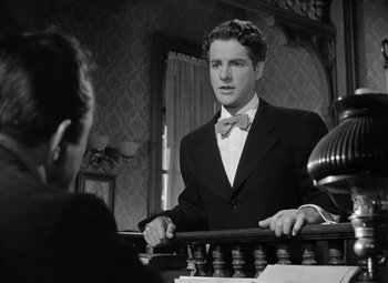 Movie still from “Kings Row” (1942), directed by Sam Wood – A man in a suit and bow tie holding a railing in front of a woman; Medium shot, Low angle