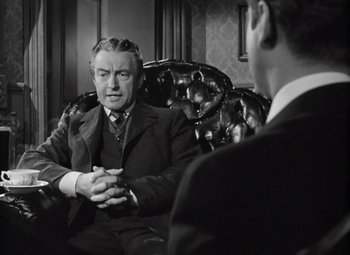 Movie still from “Kings Row” (1942), directed by Sam Wood – A man in a suit and tie talking to another man in a suit and tie; Medium shot, Over the shoulder angle