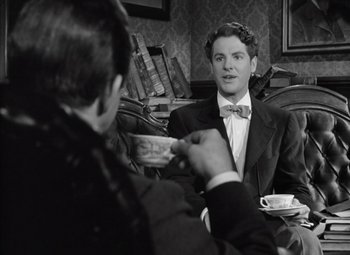 Movie still from “Kings Row” (1942), directed by Sam Wood – A man sitting at a table with another man holding a cup of coffee; Medium shot, Over the shoulder angle