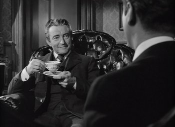 Movie still from “Kings Row” (1942), directed by Sam Wood – A man sitting in a chair holding a cup of tea; Medium shot, Over the shoulder angle