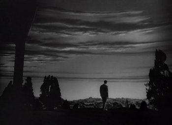 Movie still from “Kings Row” (1942), directed by Sam Wood – A man standing in front of a sky filled with clouds; Extreme Wide shot, Low angle