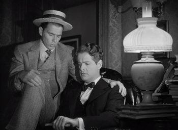 Movie still from “Kings Row” (1942), directed by Sam Wood – Two men in suits and hats are sitting in a room; Medium shot, Low angle