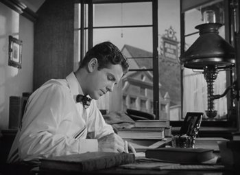 Movie still from “Kings Row” (1942), directed by Sam Wood – A man sitting at a desk writing on a piece of paper; Medium shot, Low angle