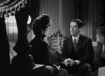 Movie still from “Kings Row” (1942), directed by Sam Wood – A man and a woman are sitting in a chair talking; Medium shot, Over the shoulder angle