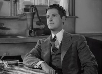 Movie still from “Kings Row” (1942), directed by Sam Wood – A black and white photo of a man sitting at a table; Medium shot, Low angle