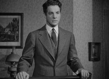 Movie still from “Kings Row” (1942), directed by Sam Wood – A man in a suit and tie standing in front of a table; Medium shot, Low angle