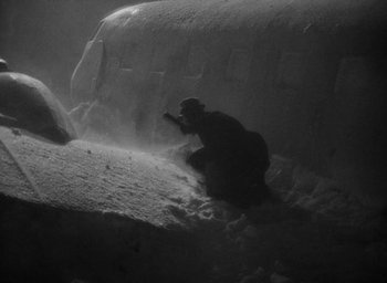 Movie still from “Lost Horizon” (1937), directed by Frank Capra – A man kneeling down in the snow near an airplane; Wide shot, High angle