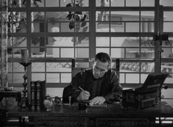 Movie still from “Lost Horizon” (1937), directed by Frank Capra – A black and white photo of a man sitting at a table writing; Medium shot, High angle