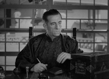 Movie still from “Lost Horizon” (1937), directed by Frank Capra – A black and white photo of a man sitting at a table writing; Medium shot, High angle