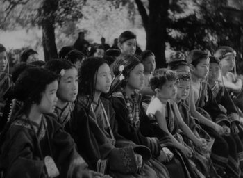 Movie still from “Lost Horizon” (1937), directed by Frank Capra – Black and white photograph of a group of people sitting in a row; Medium shot, High angle