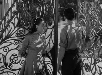 Movie still from “Lost Horizon” (1937), directed by Frank Capra – A man and a woman standing next to each other in front of an iron gate; Medium shot, High angle
