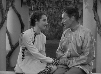 Movie still from “Lost Horizon” (1937), directed by Frank Capra – A man and a woman holding hands while sitting on the ground; Medium shot, High angle