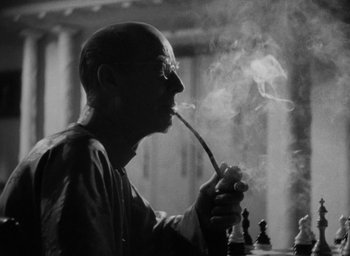 Movie still from “Lost Horizon” (1937), directed by Frank Capra – A man smoking a pipe while sitting in front of a chessboard; Close Up shot, Low angle